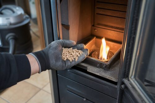 Main gantée tenant des granulés devant le foyer d’un poêle à pellets